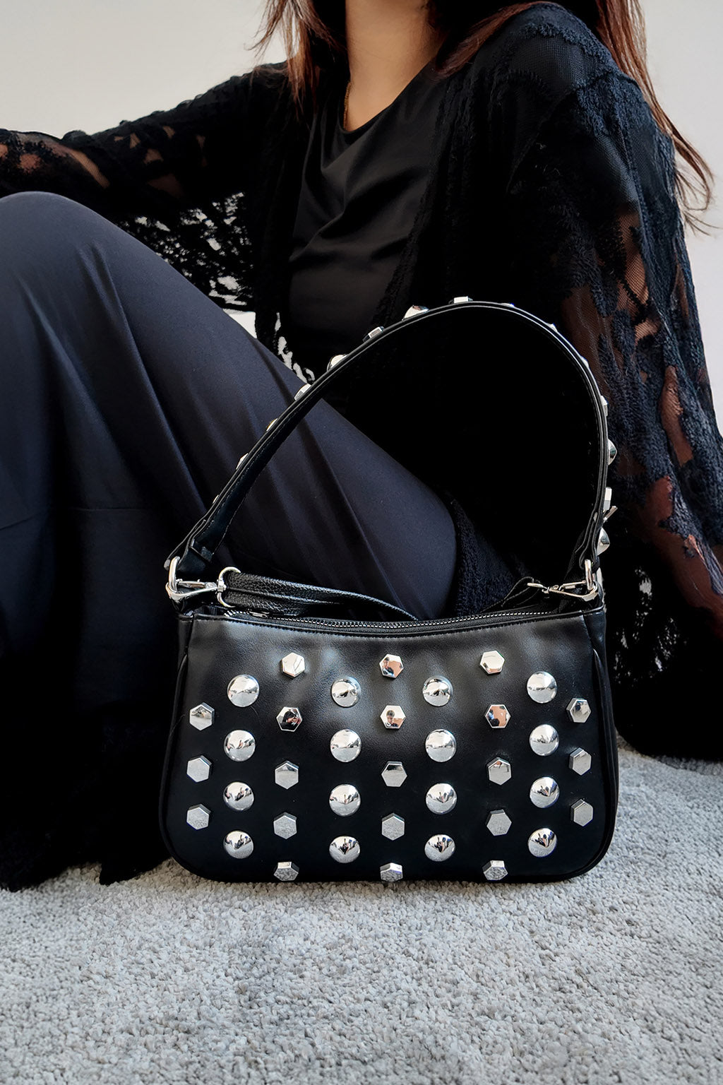 Black studded handbag on a gray carpet with a person wearing dark clothing in the background.