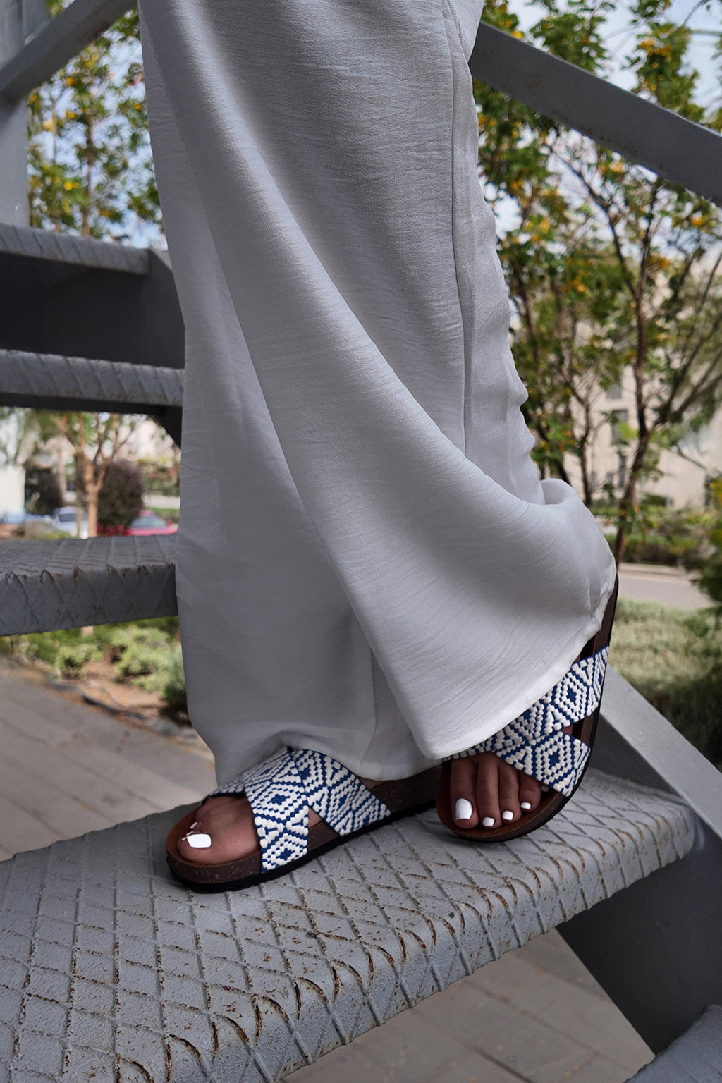 Person wearing white pants and patterned sandals on a staircase with a blurred outdoor background